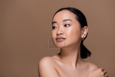 Foto de Young asian woman with naked shoulders looking away isolated on brown - Imagen libre de derechos