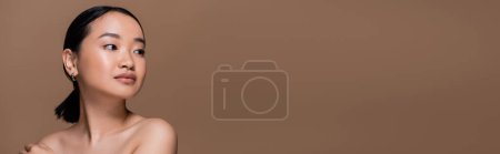 Pretty asian woman with naked shoulders looking away isolated on brown, banner 