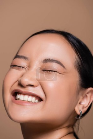 Portrait of pleased asian model closing eyes isolated on brown 