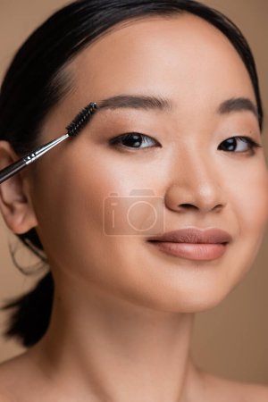 Téléchargez les photos : Portrait of young asian woman with makeup holding eyebrow brush isolated on brown - en image libre de droit