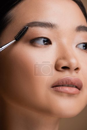 Cropped view of asian woman holding eyebrow brush isolated on brown 