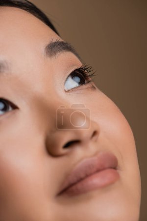 Foto de Close up view of young asian woman with visage looking away isolated on brown - Imagen libre de derechos