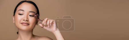 Pretty asian woman holding eyelash curler isolated on brown with copy space, banner 