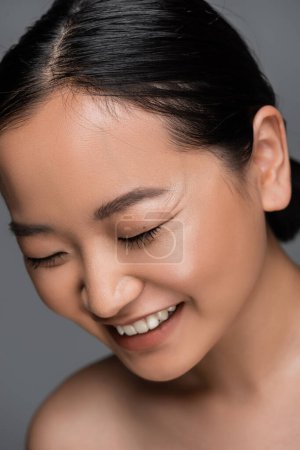 Portrait of positive asian woman closing eyes isolated on grey 