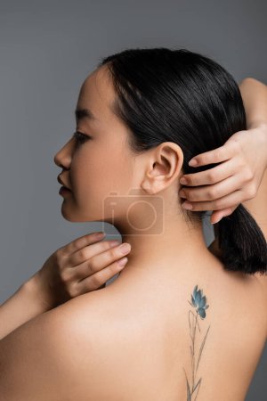 Photo for Side view of tattooed asian woman touching hair isolated on grey - Royalty Free Image
