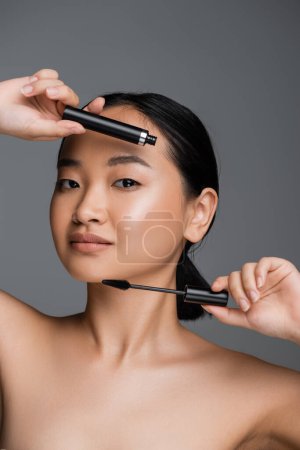 asian woman with perfect skin and natural makeup holding black mascara isolated on grey