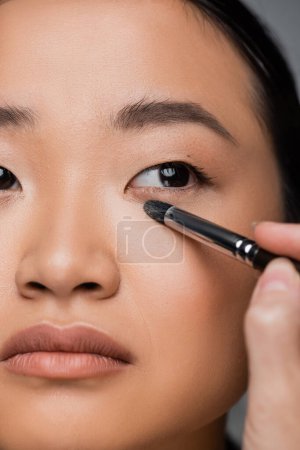 Photo for Close up view of cropped asian woman with makeup foundation applying eye shadow isolated on grey - Royalty Free Image