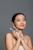 brunette asian woman with perfect skin holding bottles of natural cosmetic serum isolated on grey puzzle #632593828