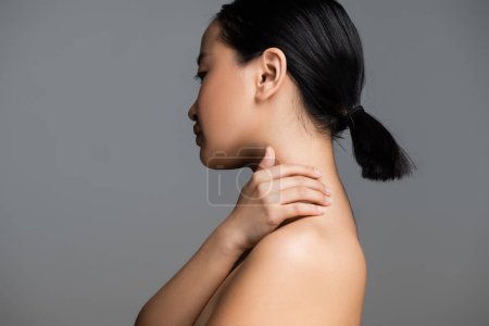 Foto de Profile of brunette asian woman with ponytail touching neck isolated on grey - Imagen libre de derechos