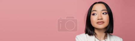portrait of brunette asian woman with makeup looking away isolated on pink, banner