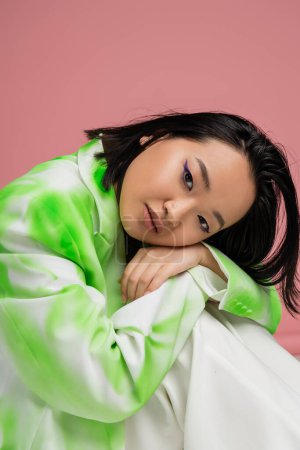 Photo for Portrait of young asian woman in green and white outfit and visage with blue eyeliner looking at camera isolated on pink - Royalty Free Image