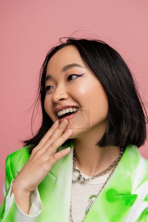 Photo for Amazed and happy asian woman with makeup touching chin and looking away isolated on pink - Royalty Free Image