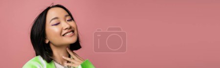 Photo for Portrait of happy asian woman with makeup and closed eyes touching neck isolated on pink, banner - Royalty Free Image