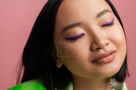 Photo for Close up portrait of pretty asian woman with perfect skin and blue eyeliner on closed eyes isolated on pink - Royalty Free Image