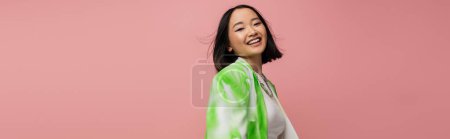 Photo for Brunette asian woman in stylish makeup and green and white blazer looking at camera isolated on pink, banner - Royalty Free Image