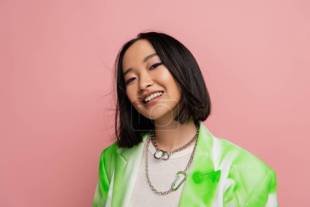 Photo for Portrait of brunette asian woman in trendy outfit and makeup looking at camera isolated on pink - Royalty Free Image