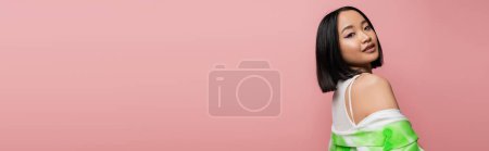 Photo for Brunette asian woman in stylish clothes looking at camera on pink background, banner - Royalty Free Image