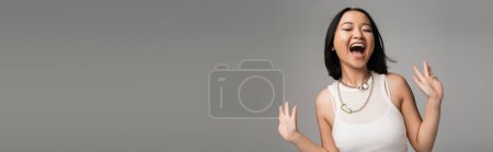 Photo for Excited asian woman in white tank top shouting with closed eyes isolated on grey, banner - Royalty Free Image