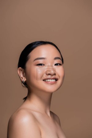 Foto de Happy asian woman with perfect skin and natural makeup looking at camera isolated on brown - Imagen libre de derechos