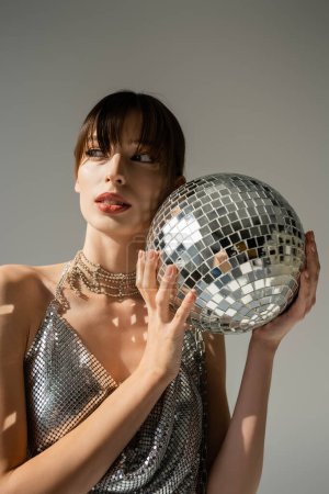 Foto de Stylish woman in shiny top holding disco ball isolated on grey - Imagen libre de derechos