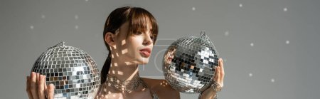 young woman holding shiny and vintage disco balls on grey background, banner 