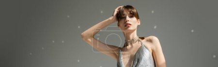 stylish woman in trendy top standing with hand near head on grey background, banner 
