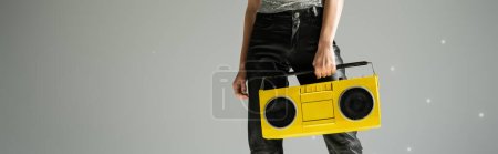 cropped view of woman in black leather pants holding boombox on grey background, banner