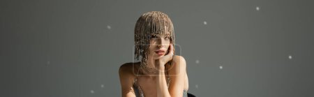 Foto de Young model with metallic headwear with jewelry looking at camera on grey, banner - Imagen libre de derechos