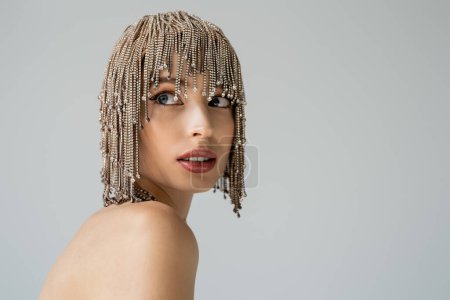 Pretty young woman with jewelry headwear and naked shoulder looking away isolated on grey  