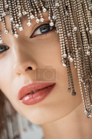 Cropped view of stylish model with makeup and jewelry headwear looking at camera isolated on grey 