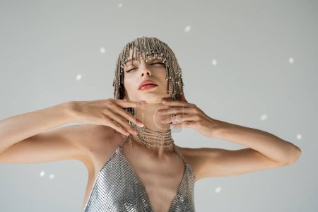 Trendy young woman in jewelry headwear touching chin on grey background with light 