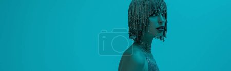 Stylish young model in jewelry headwear looking at camera isolated on blue, banner 