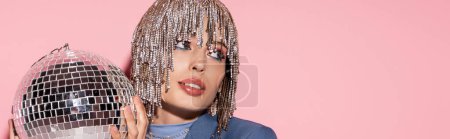 Stylish woman with makeup and jewelry headwear holding disco ball on pink background, banner 