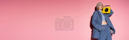 Trendy woman in jewelry headwear holding boombox on pink background with shadow, banner 