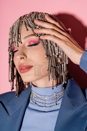 Portrait of trendy woman with makeup touching jewelry headwear on pink background 