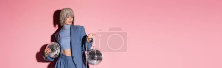 Trendy woman in luxury headwear and suit holding mirror balls on pink background, banner 