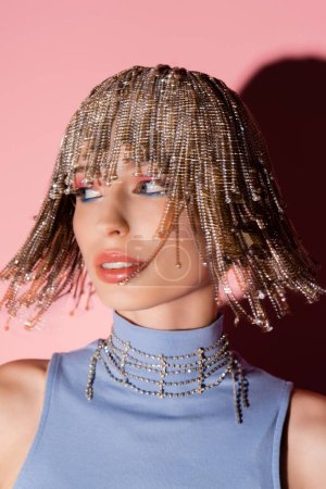 Motion blur of stylish woman in jewelry headwear looking away on pink background 