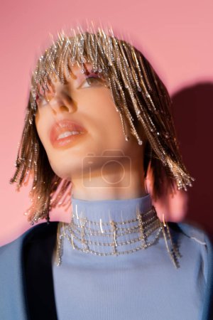 Long exposure of stylish model in jewelry headwear looking away on pink background 