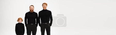 Photo for Red haired and bearded men in black clothes standing with hands in pockets near happy boy isolated on grey, banner - Royalty Free Image
