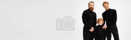 Photo for Happy bearded men and redhead boy in black clothes looking at camera isolated on grey, banner - Royalty Free Image