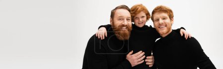Téléchargez les photos : Happy bearded men embracing red haired boy and smiling at camera isolated on grey, banner - en image libre de droit