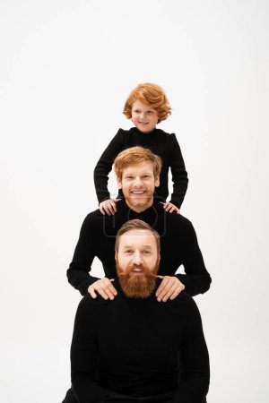 Photo for Cheerful red haired kid posing near bearded dad and grandfather in black turtlenecks isolated on grey - Royalty Free Image