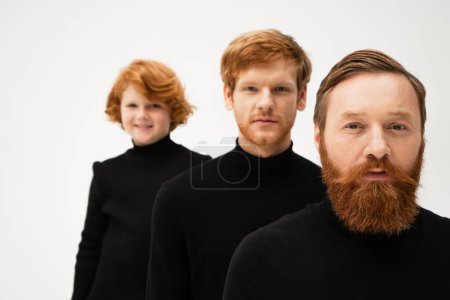 bearded redhead men and smiling boy in black sweaters looking at camera isolated on grey