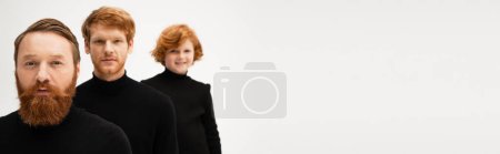 redhead boy in black turtleneck smiling at camera near father and bearded granddad isolated on grey, banner