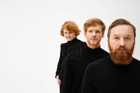 bearded man with redhead son and smiling grandson in black pullovers looking at camera isolated on grey