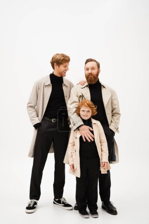 Photo for Smiling man standing with hand in pocket near bearded dad and redhead son on light grey background - Royalty Free Image