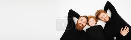 Photo for Top view of cheerful bearded man with red haired son and grandson smiling at camera while lying on light grey background, banner - Royalty Free Image