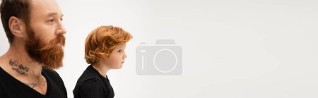 Photo for Side view of bearded tattooed man near red haired grandson isolated on grey, banner - Royalty Free Image
