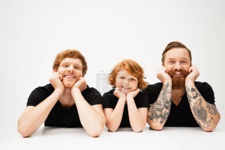 Photo for Happy boy with redhead father and bearded tattooed grandpa lying and smiling at camera on light grey background - Royalty Free Image