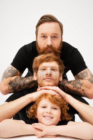 Téléchargez les photos : Family portrait of bearded tattooed man with red haired son and grandson on light grey background - en image libre de droit